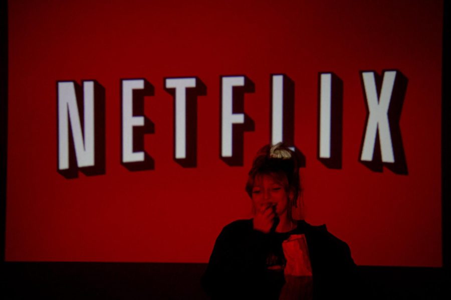 Senior Ella Lagoski eats popcorn while posing in front of a TV displaying the Netflix logo. 