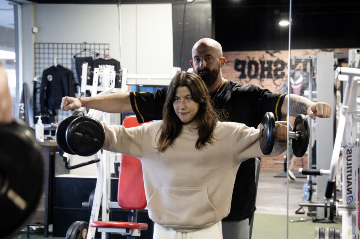 Trainer Caleb Blankenship helps senior Ella Cruz do lateral raises on Dec. 27. “[Caleb] has shown me what it’s like to like my body and how to adjust to the changes,” Ella said. “I learned that it’s important to be yourself and learn what makes you happy.”